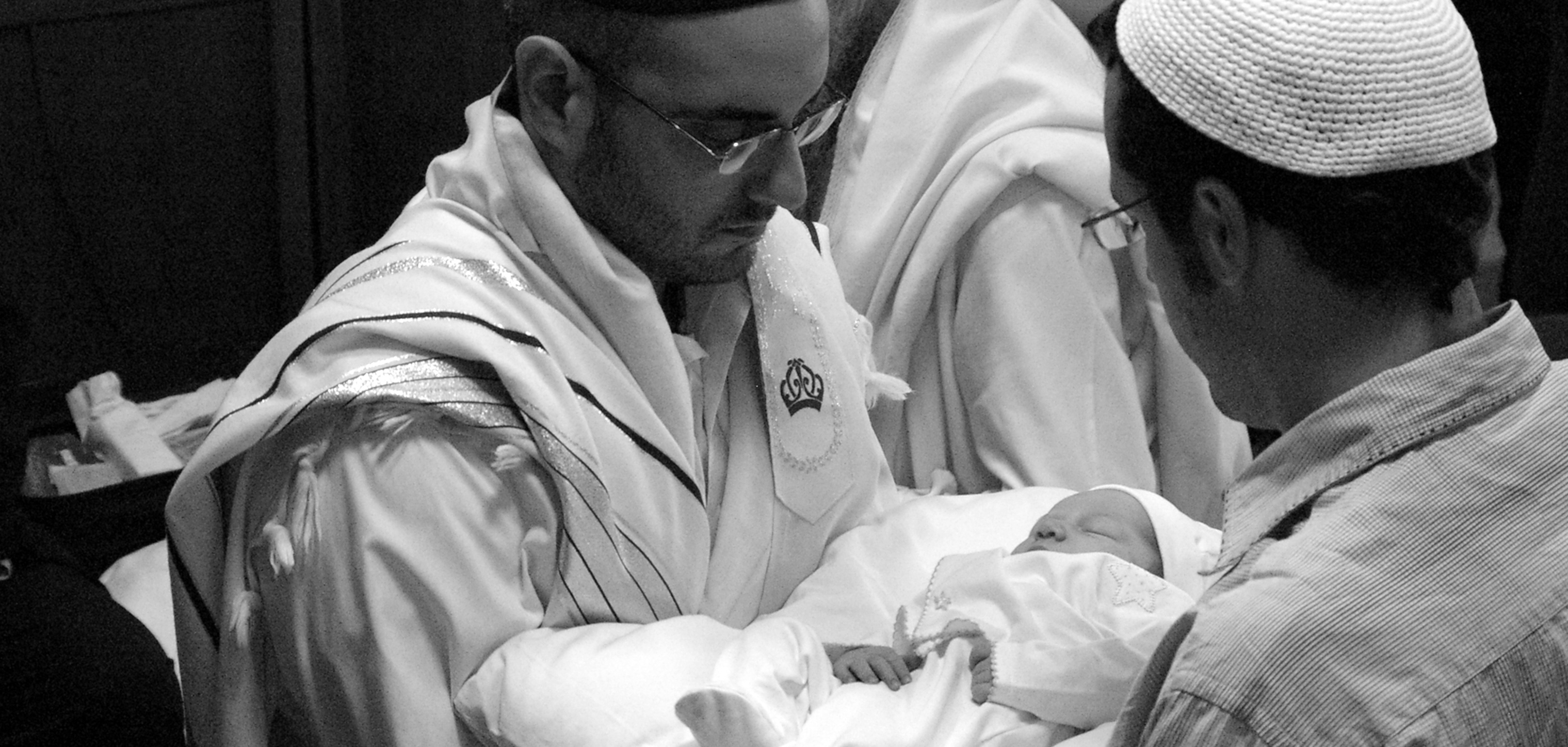 An infant is prepared for his brit milah by rabbis in a British synagogue. Photo by Yosef Silver used under Creative Commons Licence.
